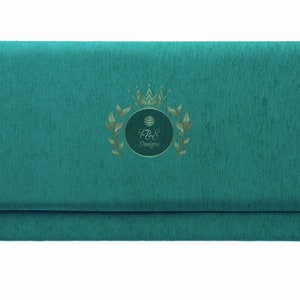 May include: Teal blue fabric envelope with a gold crown and laurel wreath design. The text "F&S Designs" is inside the wreath.
