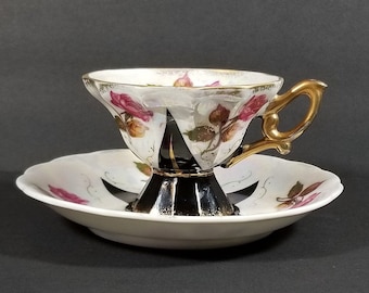 Puede incluir: Un juego de taza y platillo de té blanco con un diseño floral. La taza tiene un asa dorada y una base negra. El platillo tiene un borde festoneado.