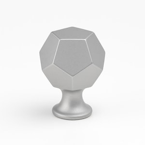 May include: A silver cabinet knob with a geometric, multi-faceted design. The knob has a rounded base and a dodecahedron-shaped top. The hardware is made of metal and is set against a white background.