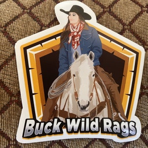 May include: A sticker featuring a cowgirl on a white horse, wearing a black hat and denim jacket. The sticker has a brown and orange border with the text "Buck Wild Rags" in a bold, stylized font.