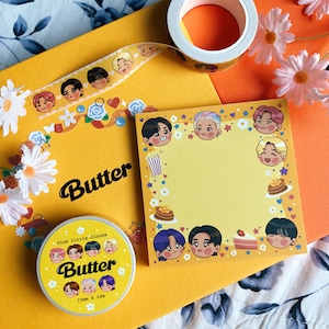 May include: A yellow notepad with a border of cartoon characters and a white background. The notepad has the word "Butter" written on it. The notepad is surrounded by yellow and orange paper and a roll of washi tape with cartoon characters on it.