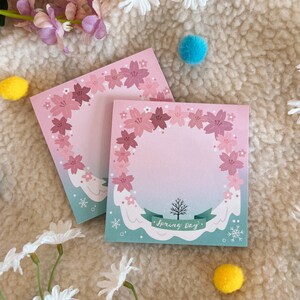 May include: Two pink and white sticky note pads with a floral design and the text "Spring Day".