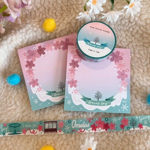 May include: Pink and blue floral patterned washi tape with the text "Spring Day" and "Omelas". The tape is next to two pink and blue floral patterned memo pads with the text "Spring Day" and a pink and blue floral patterned sticker with the text "Pink Little Clouds Spring Day 15mm x 10m".