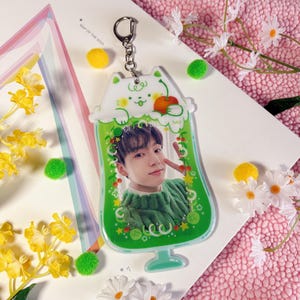 May include: A green and white keychain featuring a cartoon cat holding a red apple. The keychain has a clear plastic window with a photo of a person inside. The text "MAP OF THE SOUL" is visible in the background.