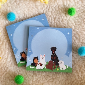 Puede incluir: Un juego de dos tarjetas de notas azules con un dise&ntilde;o de nube blanca y estrellas. Las tarjetas presentan un grupo de perros, incluyendo un perro negro y marr&oacute;n, un perro blanco, un perro negro y marr&oacute;n, un perro blanco, un perro negro y un perro blanco. Los perros est&aacute;n todos sentados o de pie en un campo verde con una pelota de tenis amarilla.