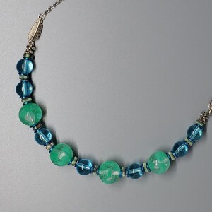 Puede incluir: Un collar con cadena plateada y detalles de plumas. Presenta cuentas turquesas y verdes alternas. Las cuentas varían en tamaño y forma, creando un diseño distintivo. Un accesorio elegante.