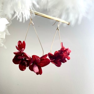 Puede incluir: Un par de pendientes colgantes con un marco de alambre en forma de lágrima y acentos de flores de papel rojo.