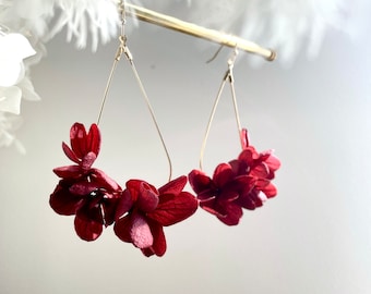 May include: A pair of dangle earrings with a teardrop-shaped wire frame and red paper flower accents.