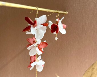 May include: A pair of dangle earrings featuring white and burgundy fabric flowers. The longer earring has a chain with a pearl at the end.