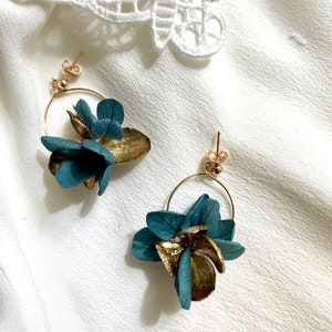 Puede incluir: Un par de pendientes de aro dorados con detalles de flores azul turquesa. Las flores est&aacute;n hechas de flores secas prensadas.
