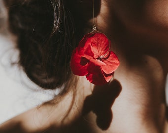 May include: A pair of gold earrings with a red flower design. The flower is made of real pressed flowers and is attached to a gold hoop.