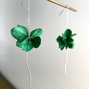 May include: A pair of silver dangle earrings with green flower accents. The flowers are made of fabric and have a delicate, realistic look.