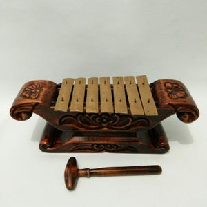 Könnte beinhalten: Ein hölzernes indonesisches Genderang, eine Art Xylophon, mit Bronzetasten. Das Instrument hat kunstvolle Schnitzereien und einen passenden Holzschlägel. Das Genderang ist ein traditionelles Schlaginstrument, das in Gamelan-Ensembles verwendet wird.