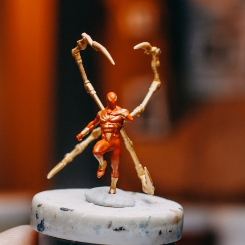 May include: A red and gold action figure of a superhero with long, spindly arms. The figure is posed in a dynamic stance, with one leg raised and the arms outstretched.