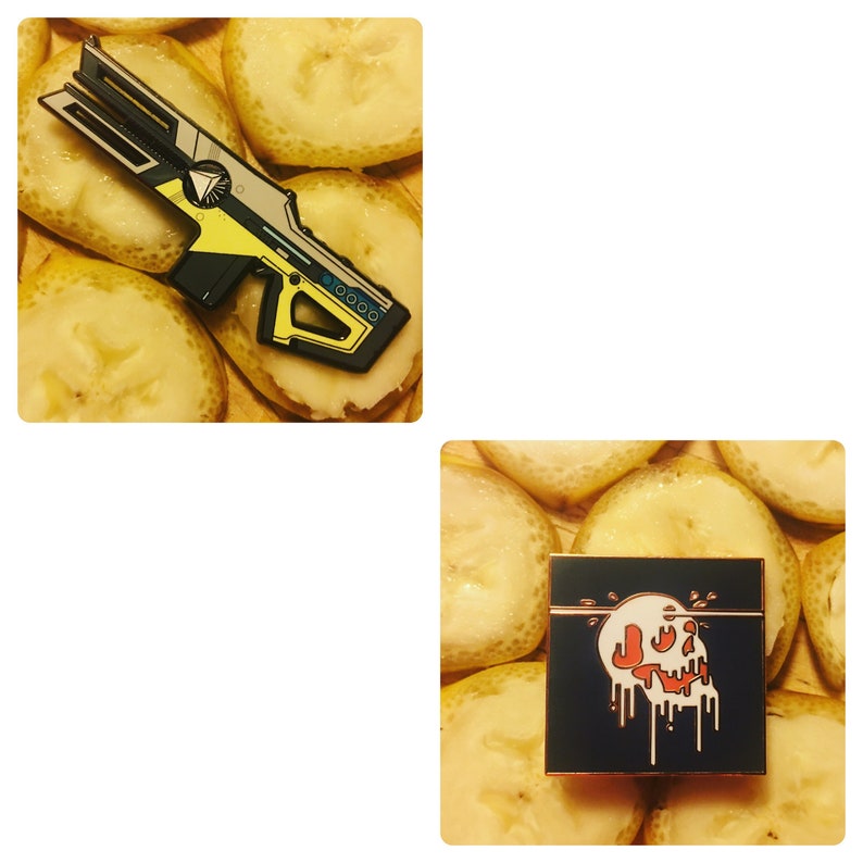 May include: Two enamel pins on a background of yellow banana slices. The first pin is a yellow and black futuristic gun. The second pin is a black square with a red and white skull dripping with red paint.