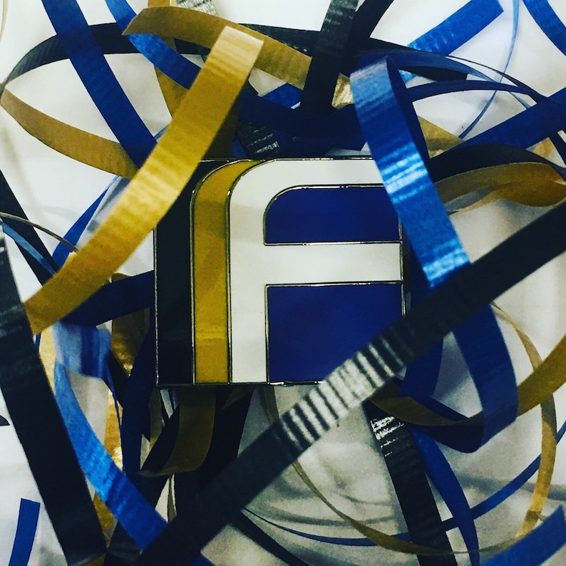 May include: A blue and white letter F pin with a gold border, surrounded by blue, gold, and black ribbon.
