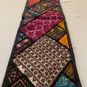 May include: A colourful table runner with a patchwork design featuring various fabrics, embroidery, and mirror accents. The runner is trimmed with black fabric.