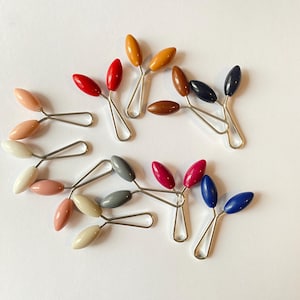 Può includere: Assortimento di clip in plastica colorate con chiusure in metallo. Le clip sono di vari colori, tra cui rosso, rosa, blu, marrone, grigio e bianco.