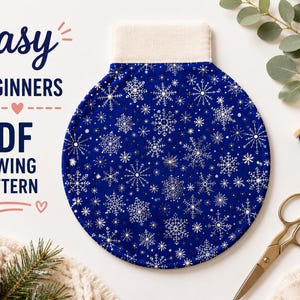 May include: A circular blue fabric ornament featuring a white snowflake pattern with a beige top tab. The text reads easy BEGINNERS PDF SEWING PATTERN. The image includes a spool of blue thread, metal scissors, and a pinecone.