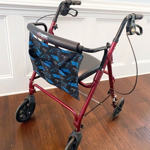 May include: A burgundy Carex rolling walker with a black seat and handles. A black and blue Carolina Panthers themed bag is attached to the front. The walker has four black wheels and is on a hardwood floor.