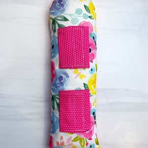 May include: A long, rectangular pillow with a floral print. The pillow has two pink pockets with white polka dots.