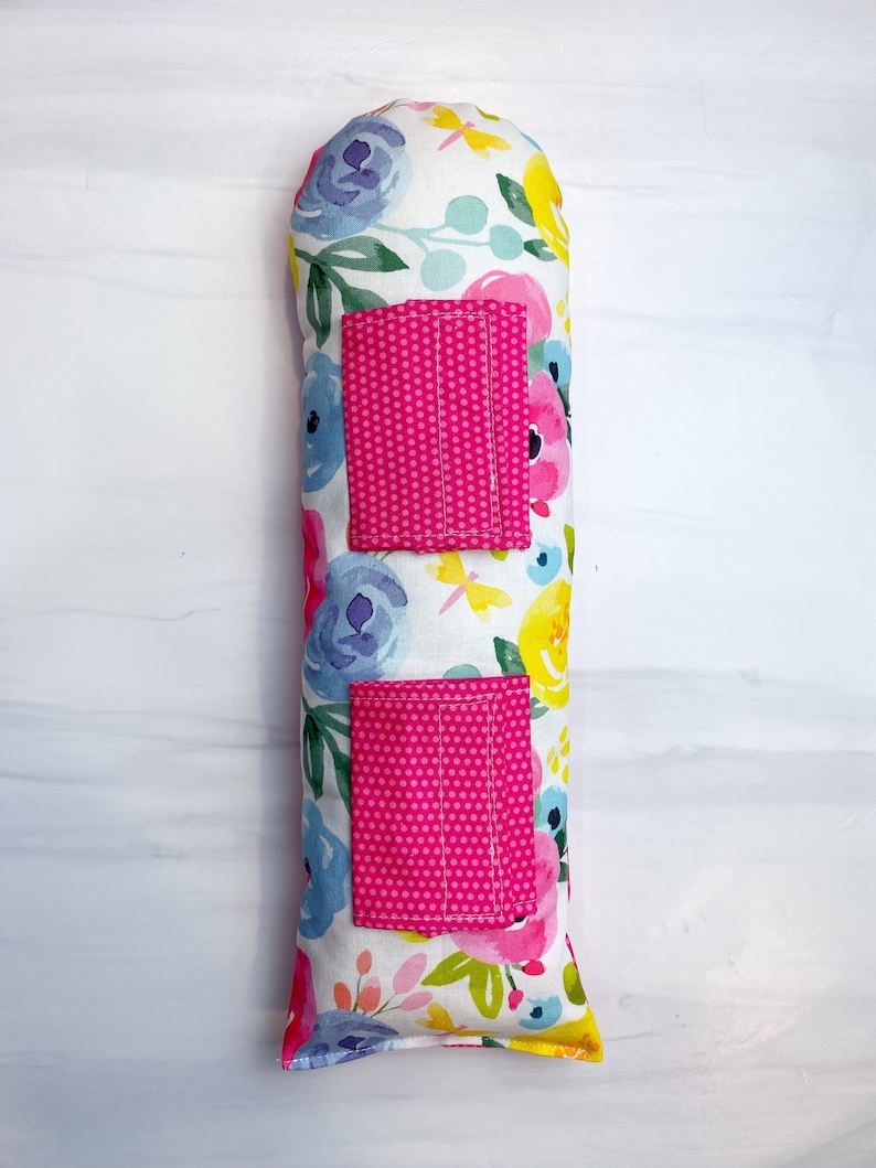 May include: A long, rectangular pillow with a floral print. The pillow has two pink pockets with white polka dots.