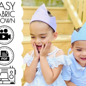 May include: Two children wearing blue and purple fabric crowns. The crowns are striped and have a pointed top. The children are smiling and looking at the camera. The image includes the text "EASY FABRIC CROWN" and icons for a video and a PDF document.