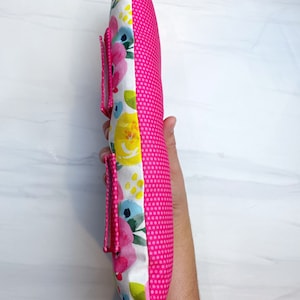 May include: A pink and white floral pillow with a pink polka dot back. The pillow has a zipper closure and a strap on the side.