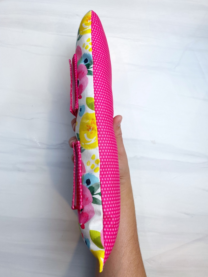May include: A pink and white floral pillow with a pink polka dot back. The pillow has a zipper closure and a strap on the side.