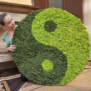May include: A large, round yin-yang symbol made of green moss. The symbol is divided into two sections of varying shades of green, with a lighter green circle in each section. The moss has a textured, natural appearance.