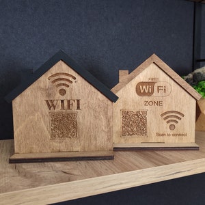 Może przedstawiać: Dwa drewniane znaki Wi-Fi w kształcie domu. Jeden znak ma czarny dach i napis "WIFI" z kodem QR. Drugi znak mówi "FREE Wi Fi ZONE" z kodem QR i "Scan to connect".