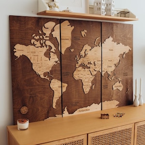 May include: A large wooden world map with a dark brown finish, mounted on a wall. The map is divided into three panels and features detailed country outlines. The map is displayed above a wooden cabinet.