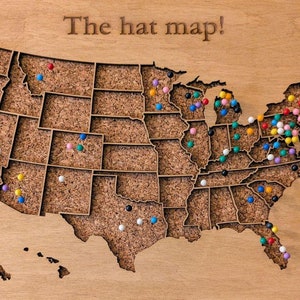May include: A corkboard map of the United States with the text "The hat map!" at the top. The map is covered in colorful push pins.