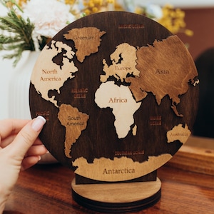 May include: A wooden world map, with continents in a lighter wood against a darker wood. The circular map is mounted on a stand. Continents are labelled. Measurements are in centimetres.