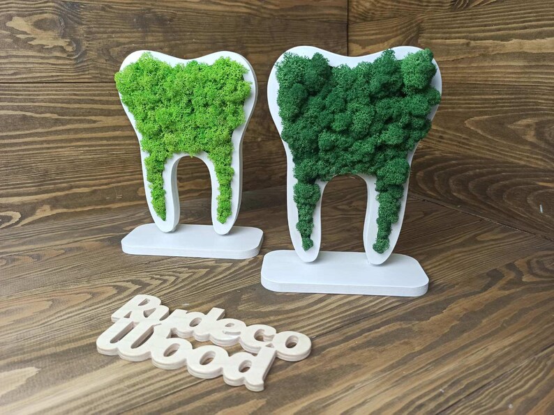 K&ouml;nnte beinhalten: Zwei wei&szlig;e, zahnf&ouml;rmige Skulpturen mit gr&uuml;nem Moos, das die Oberseite ausf&uuml;llt. Die Skulpturen stehen auf wei&szlig;en Sockeln. Das Wort "Rudeco Wood" ist in Holzbuchstaben darunter geschrieben.