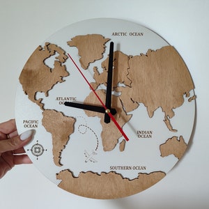 May include: A round wooden world map clock with a white background and brown continents. The clock hands are black with a red second hand. The oceans are labeled, and a small airplane graphic is included.