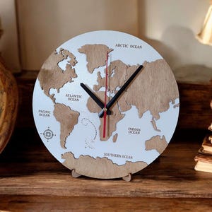 May include: A round wooden world map clock with a white face and brown continents. The clock hands are black, and the second hand is red. The oceans are labeled, and the clock is supported by a wooden stand.