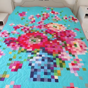 May include: A turquoise blue quilt with a pixelated floral design in shades of pink, red, green, and blue. The quilt is quilted with a wavy pattern.