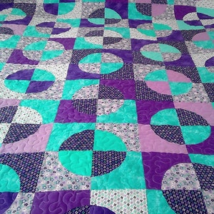May include: A quilt with a geometric pattern of teal, purple and white circles and semi-circles. The quilt is made of different fabrics with floral patterns.