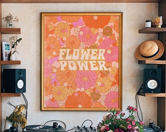 Könnte beinhalten: Ein Holztisch mit einer Vase mit rosa Blumen darauf. Der Tisch steht vor einer Wand mit einem gerahmten Druck, auf dem in einer Retro-Schrift "Flower Power" steht. Der Druck ist von einem floralen Muster in Orange-, Rosa- und Gelbtönen umgeben.
