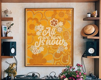 Könnte beinhalten: Ein Holztisch mit einer braunen, verwitterten Oberfläche. Eine Vase mit rosa und violetten Blumen steht auf dem Tisch. Ein gerahmter Druck mit dem Text "All we have is now" hängt an der Wand hinter dem Tisch. Der Druck hat einen gelben Hintergrund mit einem floralen Muster.