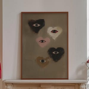 Könnte beinhalten: Ein gerahmter Druck von fünf abstrakten Herzen mit darauf gemalten Augen. Die Herzen sind in den Farben Rosa, Braun und Schwarz gehalten. Der Druck hängt über einem weißen Kaminsims in einem Raum mit einer roten Lampe und einer Kommode aus Holz.