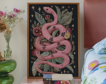 May include: A pink snake with black spots is curled around a floral design on a black background. The artwork is framed in gold and hangs above a pink bedside table with a book on top.