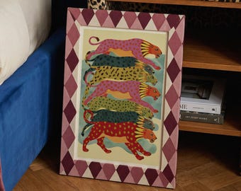 May include: A framed art print featuring a stack of colorful cheetahs. The cheetahs are in shades of pink, yellow, green, and red, with a light blue background. The frame has a diamond pattern in shades of pink and burgundy.