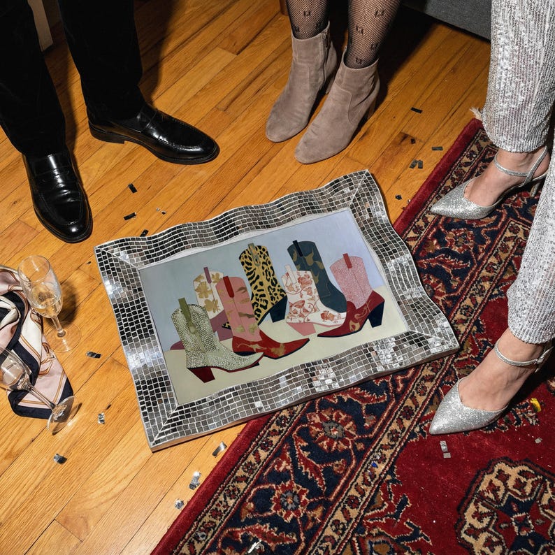 May include: A framed artwork featuring a collection of colorful cowboy boots. The boots showcase various patterns and colors, including leopard print, floral designs, and solid hues. The frame is covered in small, reflective mirrored tiles.