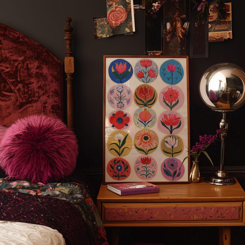 May include: A framed artwork featuring colorful floral designs in circular patterns hangs above a nightstand. A fluffy pink pillow rests on a bed with a burgundy velvet headboard. A silver lamp and a small vase with flowers are on the nightstand.