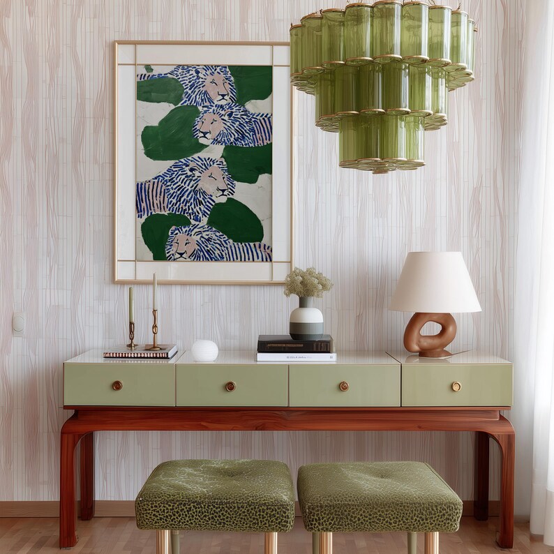 May include: A stylish interior scene featuring a green and wood console table with drawers, topped with decor. Above, a framed artwork depicts lions. Two green patterned stools sit below. A green glass chandelier hangs from the ceiling.