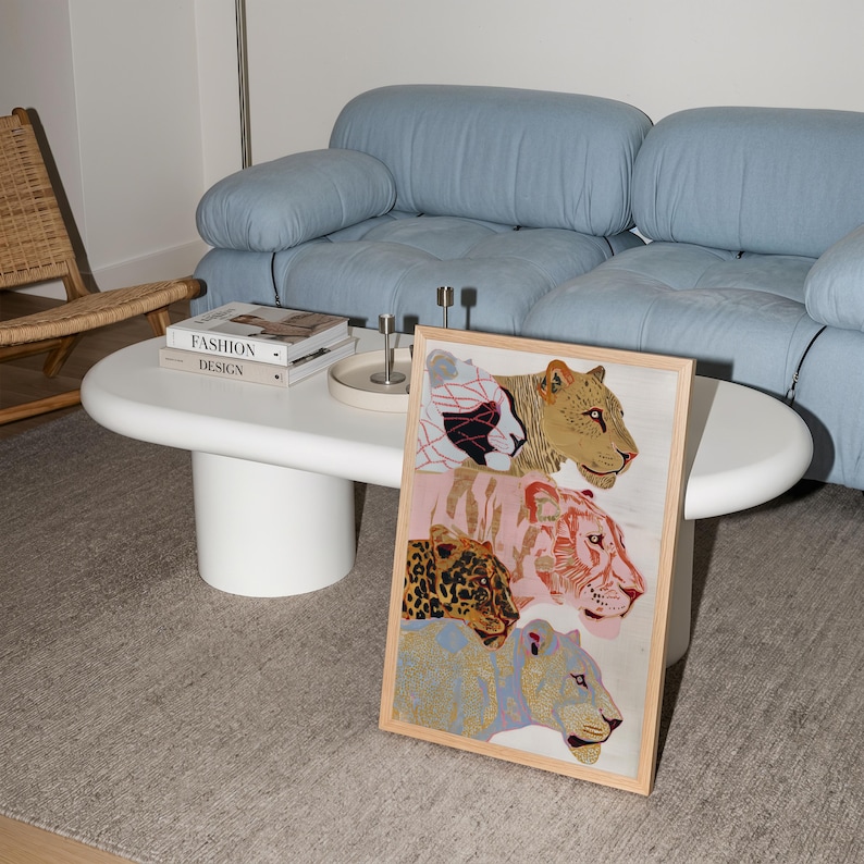 May include: A rectangular framed wall art print featuring four stacked stylised big cats. The top cat is white with black and red geometric patterns, followed by a golden-brown cat, a pink tiger, and a blue leopard with gold spots.