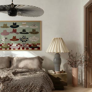 May include: A bedroom scene featuring a bed with leopard print bedding, a framed artwork of various hats, and a lamp with a pleated shade. The lamp has a black and white striped base. A vase with flowers sits on a wooden nightstand.