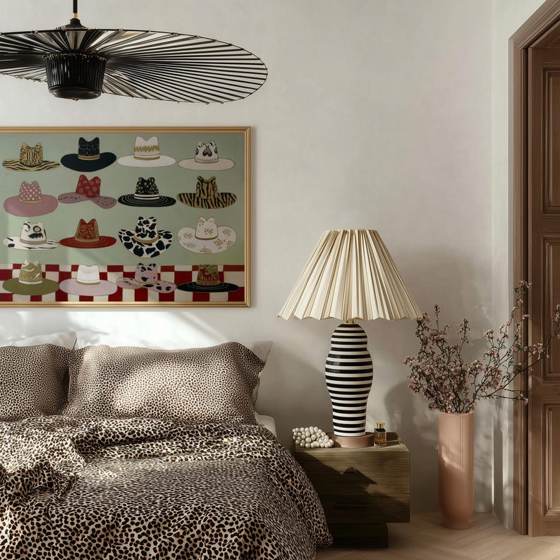 May include: A bedroom scene featuring a bed with leopard print bedding, a framed artwork of various hats, and a lamp with a pleated shade. The lamp has a black and white striped base. A vase with flowers sits on a wooden nightstand.